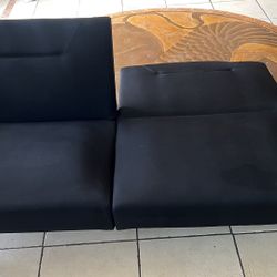 A modern sofa bed / futon with soft black fabric and peg legs