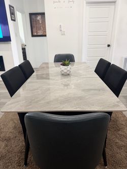 This is a modern faux-marble sintered stone dining table paired with black upholstered chairs.