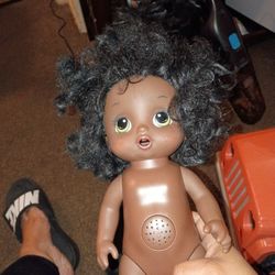 The doll in the image is a Baby Alive African American doll with black curly hair and green eyes, produced by Hasbro. 