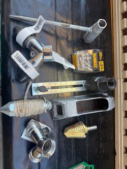 Assortment of hardware, tools, and plumbing fixtures arranged on a dark surface, including a DEWALT accessory