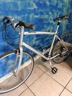 This is a silver Specialized Sirrus hybrid fitness bicycle featuring an aluminum frame and a triple crankset.