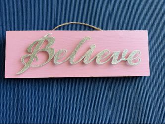 A pink wooden table decor sign featuring gold glitter "Believe" lettering, $30 or best offer