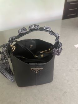 Black pebbled bucket bag. Features a top handle with a bandana-style scarf accent and a detachable crossbody strap. It has a zippered interior