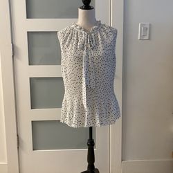 DKNY sleeveless blouse with a pleated design and polka dot print, featuring ruffle details at the neck and an adjustable tie.