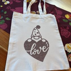 Stylish white tote bag. Features a glittery heart with 'love' text and a gnome. Perfect for casual outings. New. Hand made by me. 