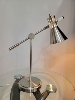 Table lamp featuring an adjustable conical head and a circular base, with an articulated or balanced-arm design; available in a brushed steel or chrom