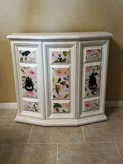 White cabinet with floral panels and decorative handles
