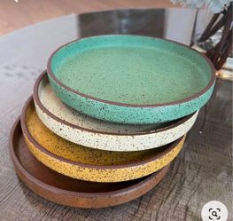 handmade ceramic plates and shallow bowls with speckled glazes in earthy and pastel tones.