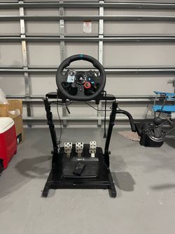 racing simulator cockpit features a Logitech G29 steering wheel mounted on an adjustable metal stand.