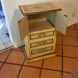 small, hand-painted accent cabinet or chest of drawers, often referred to as a jewelry armoire or lingerie chest