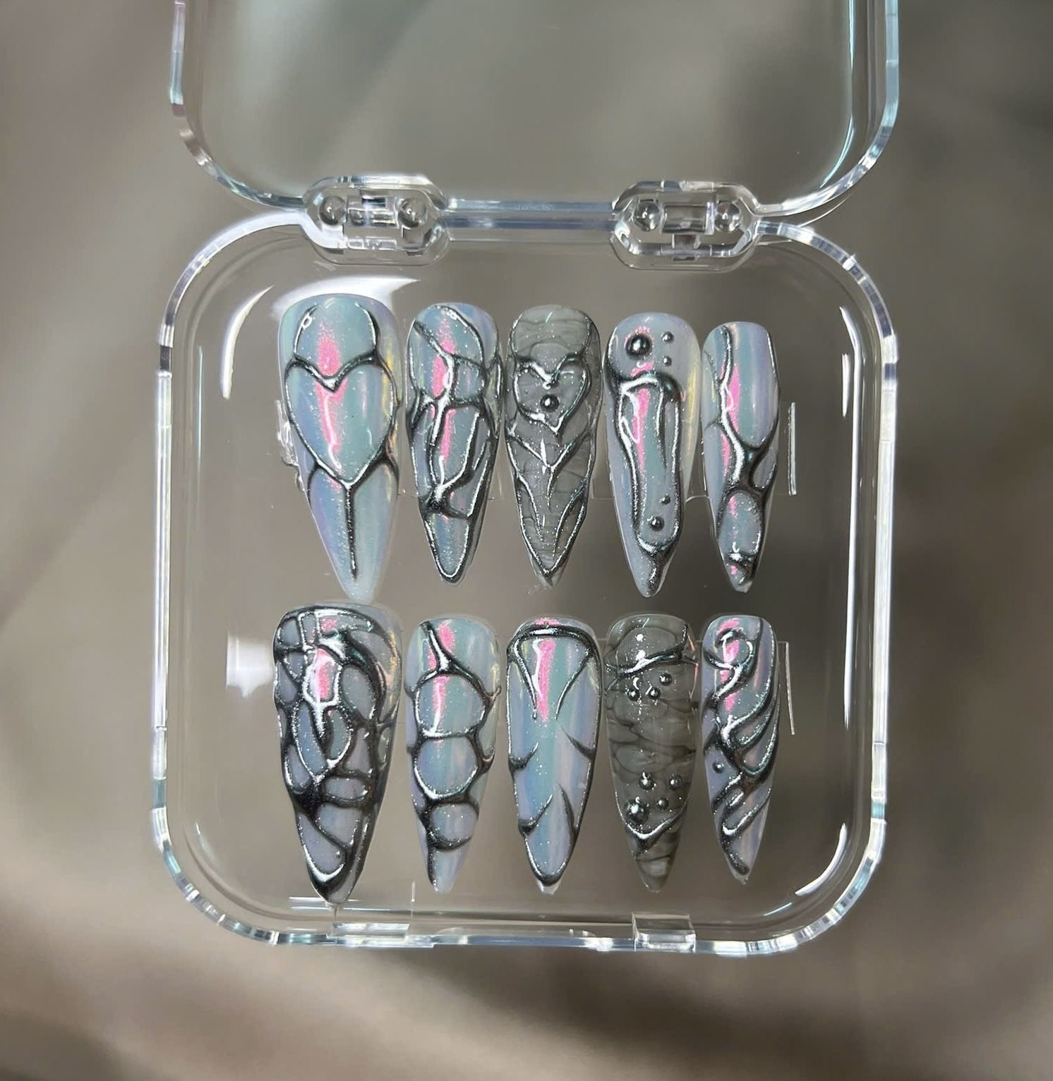 Bold and striking, this long stiletto press-on nail set features a deep black and silver ombré base with metallic chrome abstract lines and raised 3D 