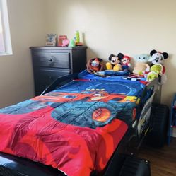 The children's bed is shaped like a monster truck and features a themed design that includes large wheels and a headboard with storage.