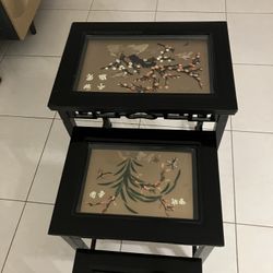 This vintage set of four Oriental nesting tables features black lacquered frames and glass tops covering decorative scenes made with inlay materials l