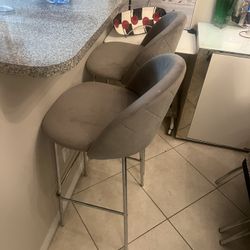 Set Of Two Grey velvet counter or bar stools with a chrome metal base.
