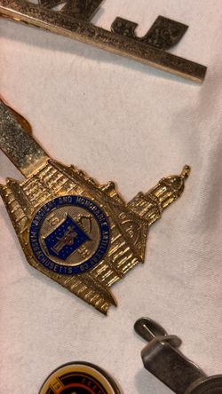 vintage gold-tone pin is a tie bar or lapel pin associated with the Ancient and Honorable Artillery Company of Massachusetts, featuring a blue enamel 