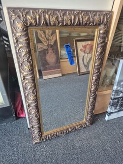 ornate vintage rectangular wall mirror with a dark bronze and gold-gilded, scroll-carved frame.