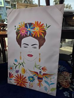 The decorative wall canvas features a colorful illustrated portrait of Frida Kahlo adorned with tropical flowers and a hummingbird.