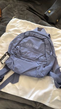 This is an adidas Linear 3 Mini Backpack in a light purple color with a front zipper pocket.