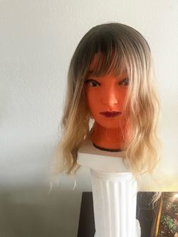 Synthetic hair wig has a dark brown to ash blonde ombre color transition. The hair is styled with loose waves and face-framing curtain bangs. It has a
