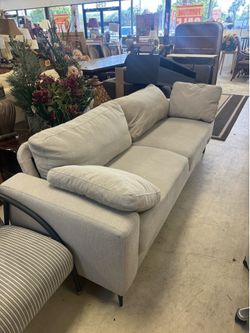 beige sofa features a contemporary, textured fabric design with sleek dark legs and plush cushions.