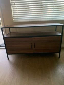 Modern industrial media console with a black metal frame and walnut-toned wood grain finish. This unit has two open shelves for electronics or decor a