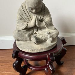Volcanic Ash Nemaste Monk With Slightly Lowered Head On Top Of A Wooden Stand 
