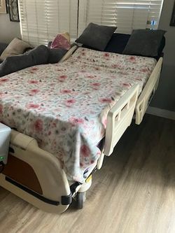 Drive-branded electric hospital bed with adjustable positioning motor unit visible at the foot of the bed. Cream-colored frame with side rails. Motor 
