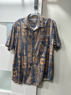 blue and tan Salty Crew block-print button-up shirt featuring marine graphics like fish and ocean waves with a chest pocket and branded woven label.