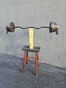💯 pounds Weight Weight plates over Black EZ curl bar loaded with cast iron weight plates on both ends, secured with spring collars. Plates show wear