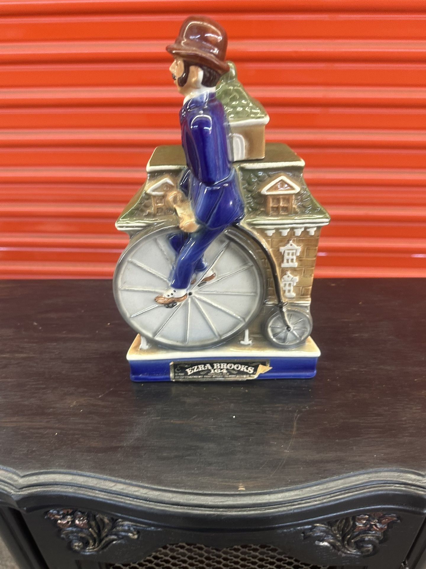 The image shows an Ezra Brooks Penny Farthington Bicycle Decanter, a vintage collectible from 1972. These decanters were designed to hold and dispense