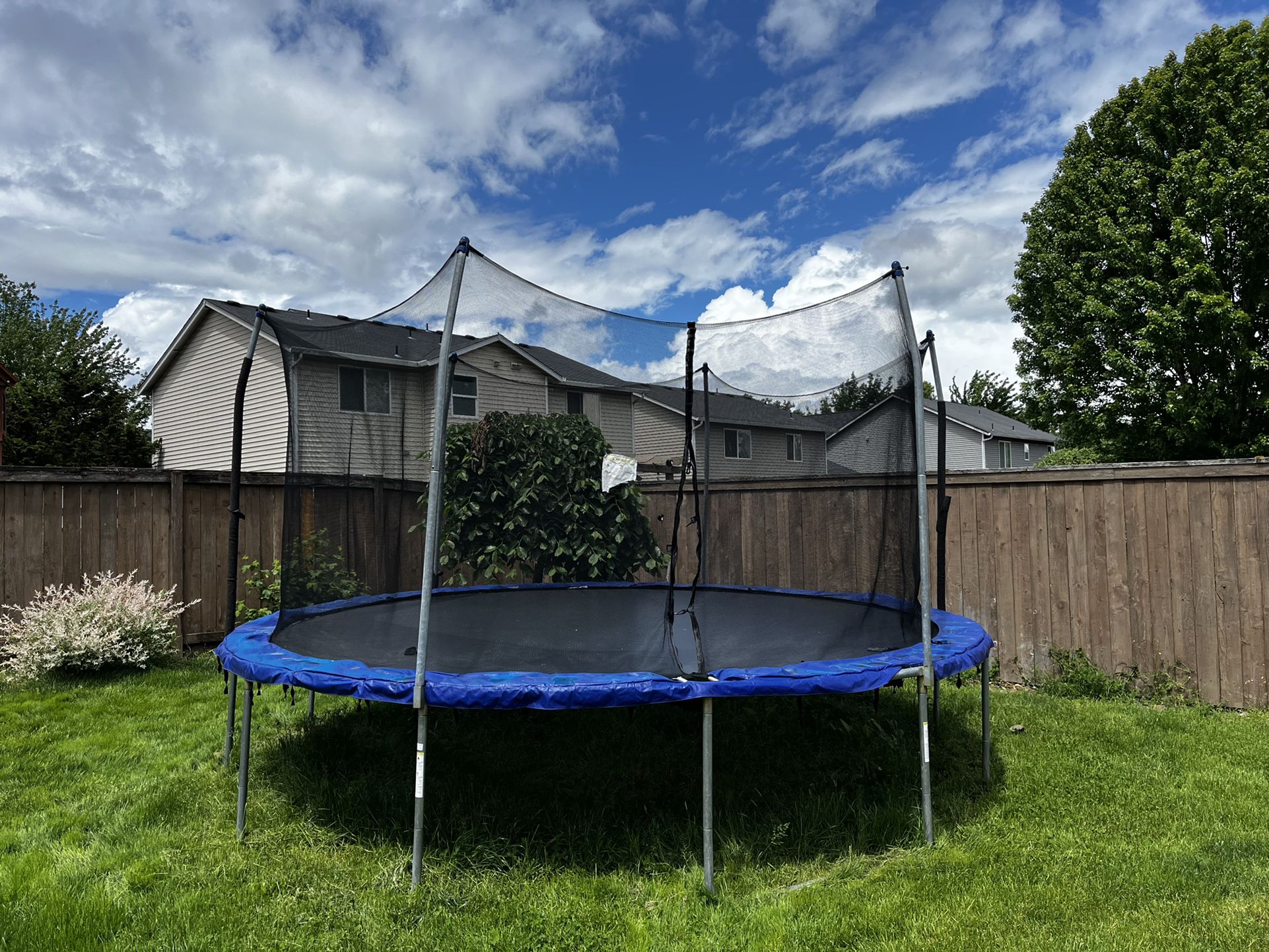 A 15 ft Skywalker Trampoline in a backyard under partially cloudy skies. 