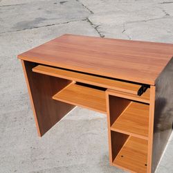 brown wooden computer desk featuring apull-out keyboard tray and built-in shelving on the right side.