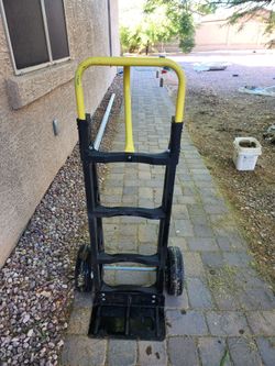 Sturdy hand truck has yellow metal handle and black plastic frame. It features two large pneumatic tires and black metal base plate. Dolly is designed