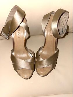 Arezzo brand sandals stand out for their sophisticated gold tone and crisscrossing straps. Elegant style with a high heel. Adjustable ankle strap. Met