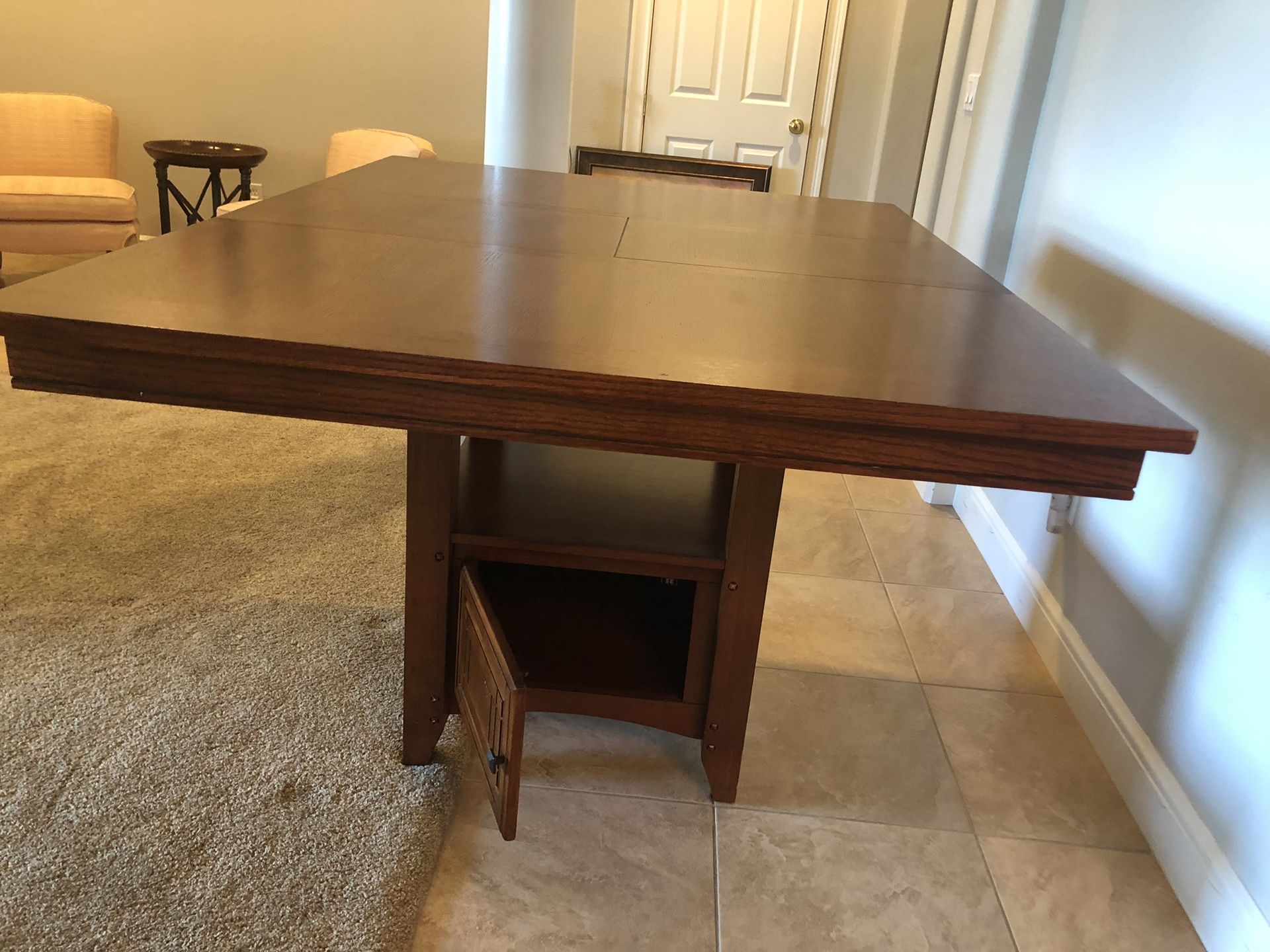 Bar height wood dining table. Can be square 48”x48” or rectangle with a middle leaflet. It has a storage and shelf under and is used but as good as n