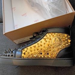 Christian Louboutin "No Limit" High-Top sneakers feature black leather, gold-tone spiked embellishments, and a signature red sole.
