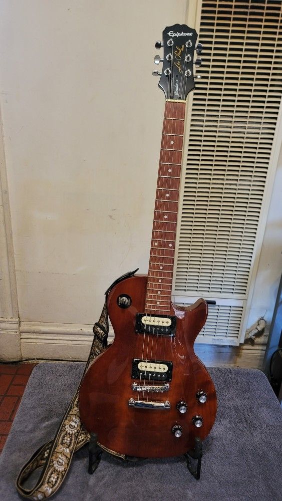 EPIPHONE LES PAUL STUDIO LT ELECTRIC GUITAR WITH DUAL IPHONE ZEBRA COIL HUMBUCKER IN WALNUT COLOR.