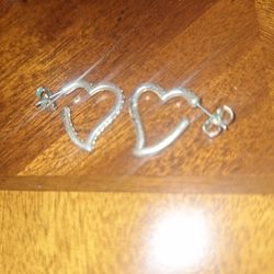  silver-colored heart-shaped hoop earrings, likely made of sterling silver or surgical stainless steel, with small clear stones lining the fr