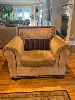 This traditional oversized golden-brown textured armchair features classic rolled arms and dark nailhead trim accents