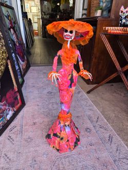 Handmade papier-mâché Catrina, dressed in an elegant long gown and a hat in shades of fuchsia and orange with a rose print.