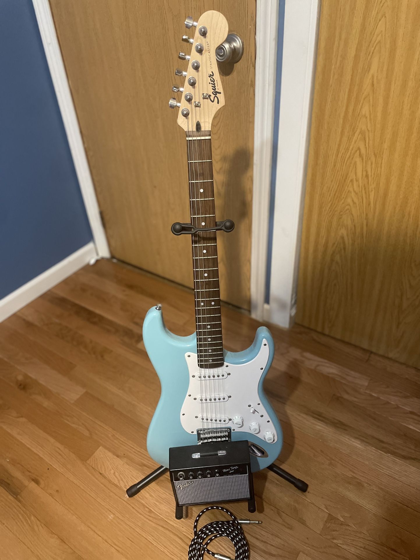 Light Blue Fender Stratocaster with guitar holder, mini amp, and amp cord