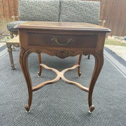 Elegant vintage wooden side table with ornate carvings and a single drawer with brass hardware. 