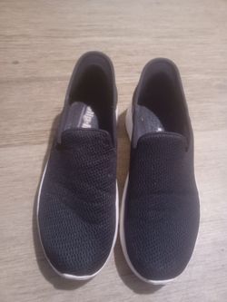 These are black Skechers GOwalk slip-on sneakers featuring a breathable mesh upper and white cushioning soles