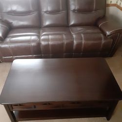 ALMOST NEW DARK LEATHER COUCH RECLINER ON EACH END AND A MAHOGANY COFFEE TABLE WITH 2 DRAWERS 