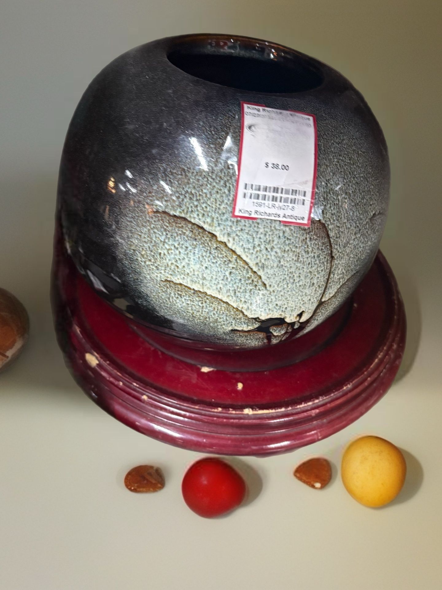 ceramic vase with a speckled or "fat lava" style glaze and a relief pattern, presented on a wooden stand
