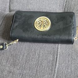 Black faux leather wristlet wallet has gold-tone hardware and a circular filigree design on front. It features a zip-around closure with two main comp