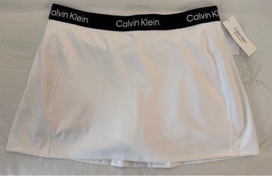 This is a Calvin Klein Performance A-Line Logo Skort in white featuring a contrasting black elastic logo waistband. Size LARGE