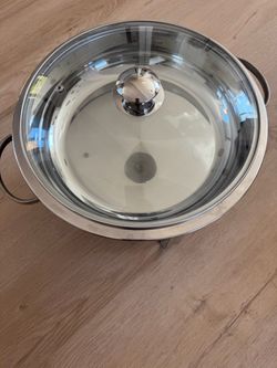 polished stainless steel round chafing dish with a glass lid and a circular base stand.