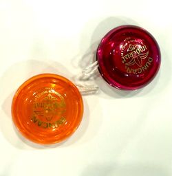 Two Duncan Imperial yo-yos in transparent pink and transparent orange. Both have gold logo imprints and white string attached.