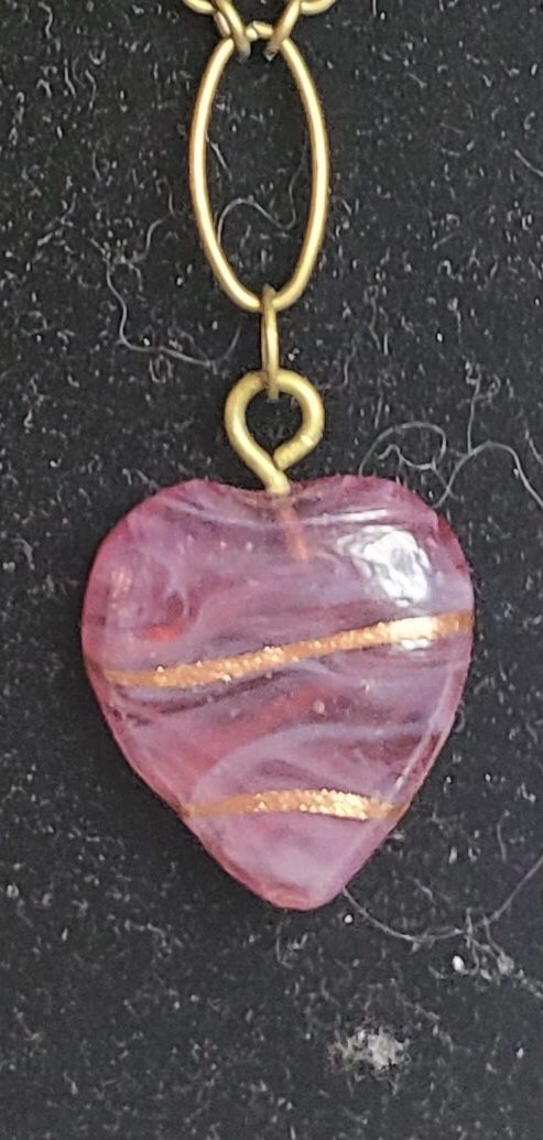 Pendant necklace made with a pink glass heart with tiny gold lines.  Chain has antiqued brass finish. Accessorized with pink ceramic beads.